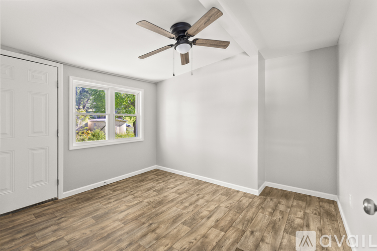 A room with a ceiling fan and a window showing a view of trees and a house.