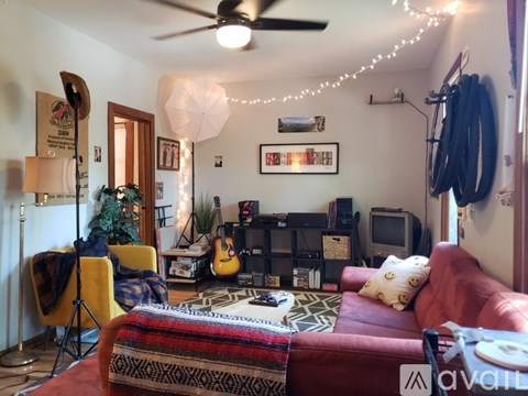 A living room with a red couch, a guitar, a television, and a ceiling fan.