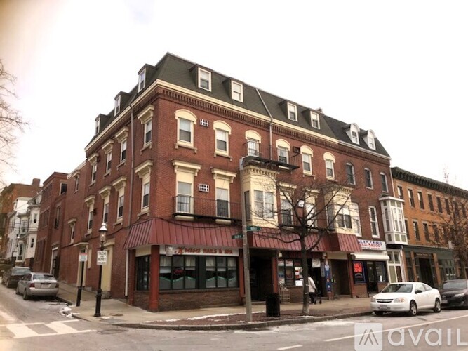 A street view of a red brick building with a green awning and a white car parked in front.