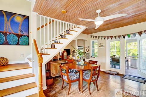 A wooden staircase with a white railing leads to a living room with a dining table and chairs.