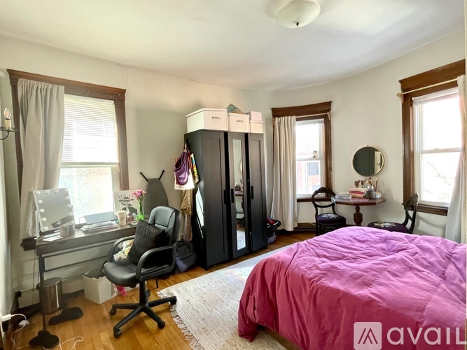 A bedroom with a pink bedspread and a black chair.