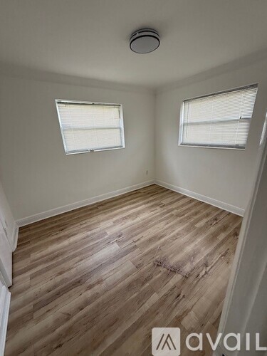 A room with wooden flooring and two windows.