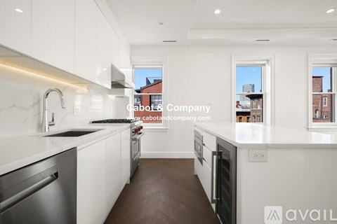 A modern kitchen with white cabinets and a view of a red building outside the window.