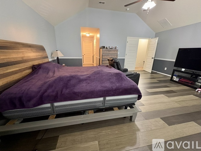 A bedroom with a bed covered in a purple blanket and a ceiling fan.