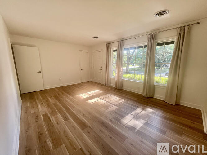 A spacious room with wooden flooring and a large window with curtains.