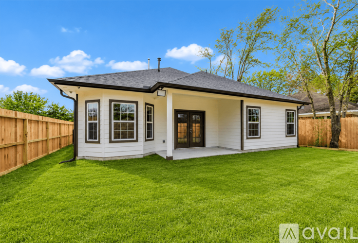 A house with a white exterior and a black roof is surrounded by a green lawn.