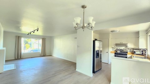 A well-lit, spacious kitchen and living room with a chandelier and a refrigerator.