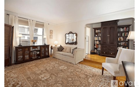 A living room with a couch, a chair, a rug, and a bookshelf.