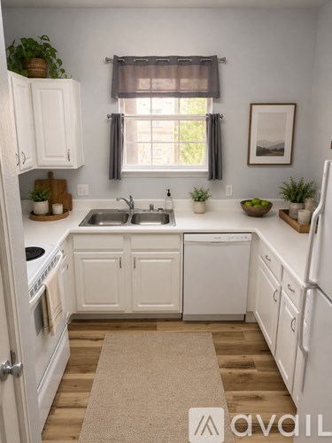 A kitchen with white cabinets and appliances, a window with a plant on the windowsill, and a rug on the floor.