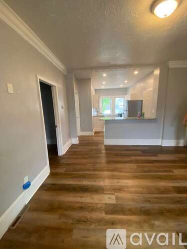 A room with wooden flooring and a kitchen area in the background.