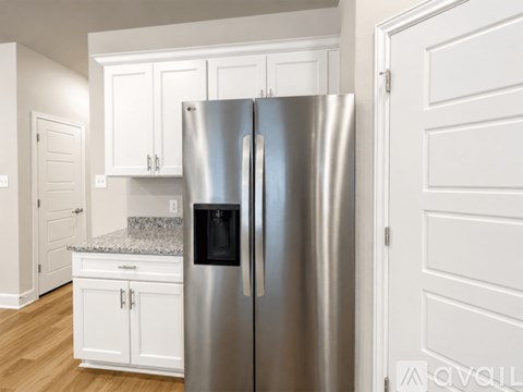 A stainless steel refrigerator stands in a kitchen with white cabinets.