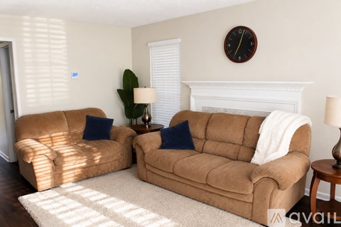 Two tan couches in a living room with a clock on the wall.