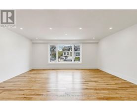 A spacious room with wooden flooring and a large window showing a street view.