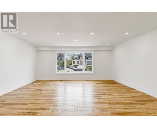 A spacious room with wooden flooring and a large window showing a street view.