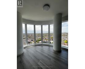 A real estate listing image of a room with a large window overlooking a city.