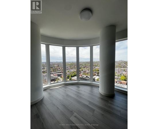 A real estate listing image of a room with a large window overlooking a city.