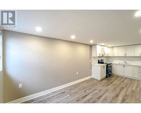A well-lit, empty room with a kitchenette and wooden flooring.