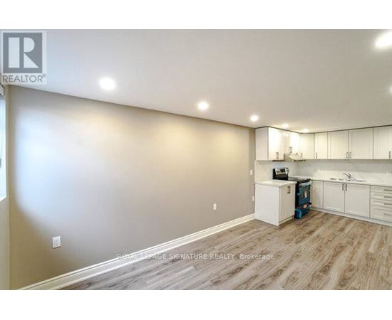 A well-lit, empty room with a kitchenette and wooden flooring.