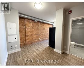 A room with a brick wall and a black refrigerator.
