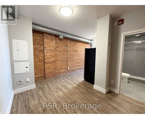 A room with a brick wall and a black refrigerator.
