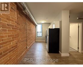 A hallway with a brick wall on the left and a black refrigerator on the right.