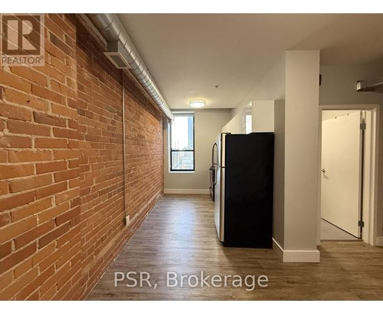 A hallway with a brick wall on the left and a black refrigerator on the right.