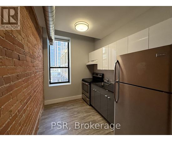 A kitchen with a stainless steel refrigerator and wooden flooring.