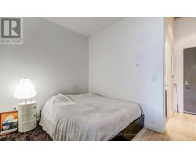 A bedroom with a bed, lamp, and a framed picture on the floor.