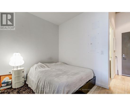 A bedroom with a bed, lamp, and a framed picture on the floor.