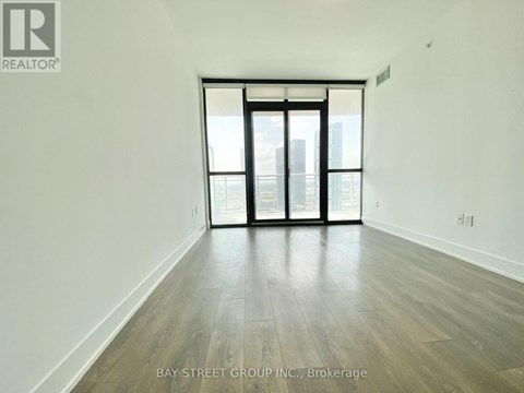 A spacious room with wooden flooring and large windows overlooking a cityscape.