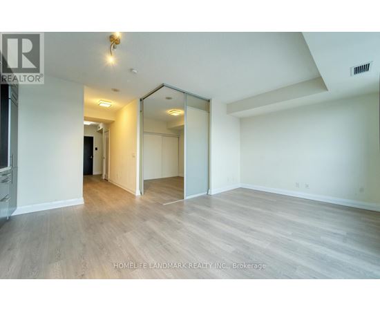 A spacious room with wood flooring and a large mirror on the wall.