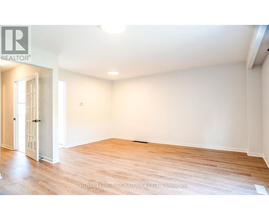 A room with wooden flooring and white walls, with a door on the left side.
