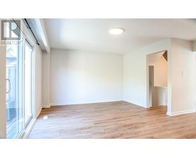 A room with wooden flooring and white walls, with a doorway leading to another room.