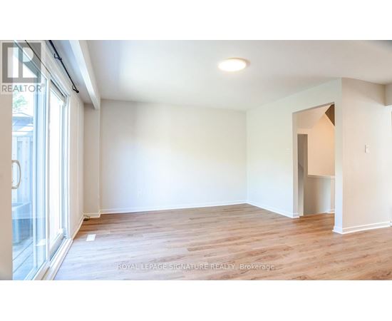 A room with wooden flooring and white walls, with a doorway leading to another room.