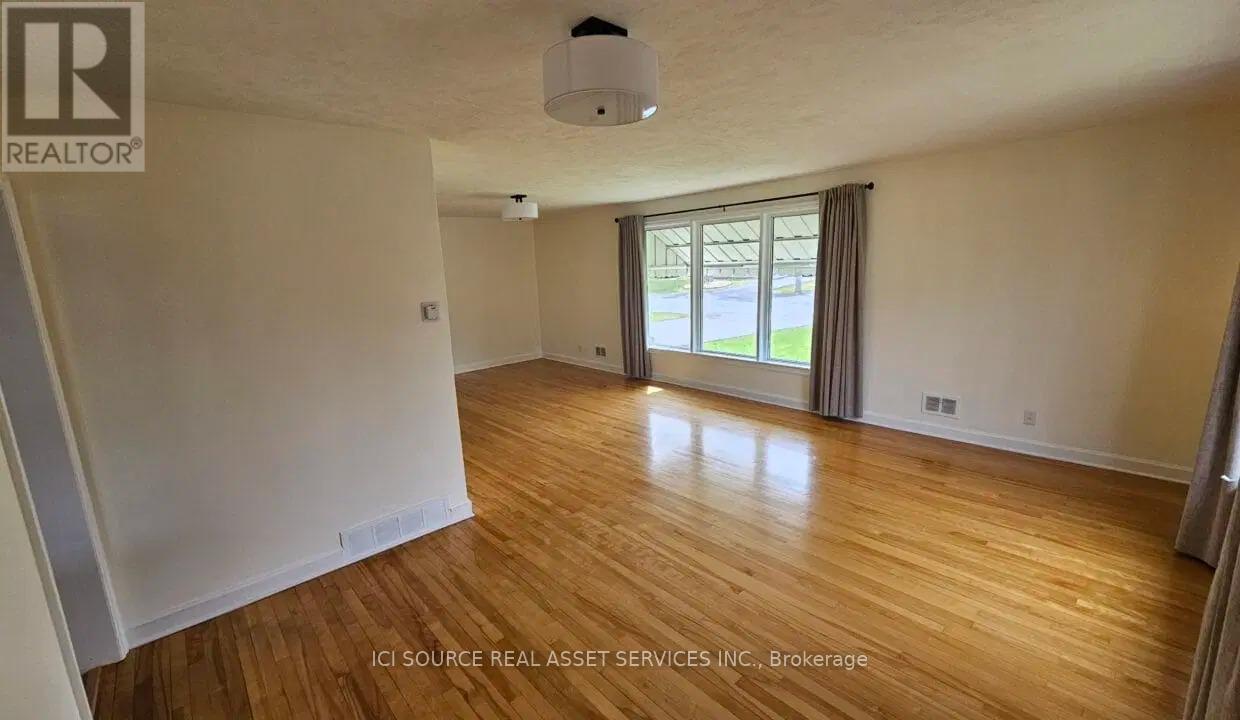 A room with wooden floors and a window with a view of a green area outside.