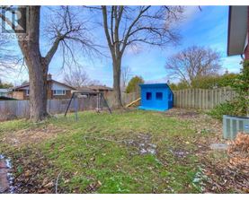 A blue shed sits in a backyard with a wooden fence and bare trees.