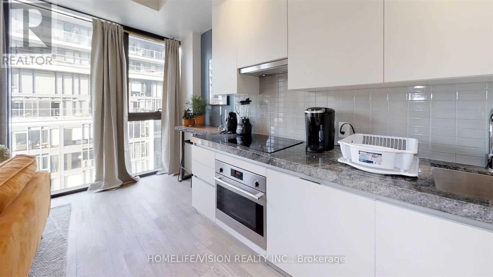 A modern kitchen with white cabinets and a large window.