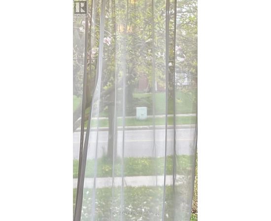 A view of a street through a window with a curtain.