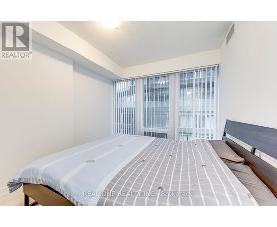 A bedroom with a bed and a window with blinds.
