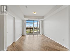 A spacious room with wooden flooring and a large window overlooking a green area.