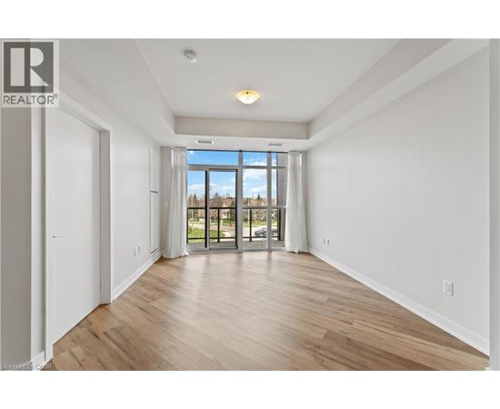 A spacious room with wooden flooring and a large window overlooking a green area.