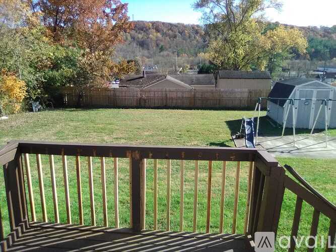 A wooden deck overlooks a backyard with a fence and trees.