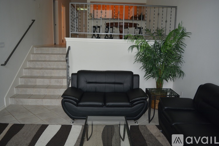 A black leather sofa sits in a living room with a striped rug and a potted plant.