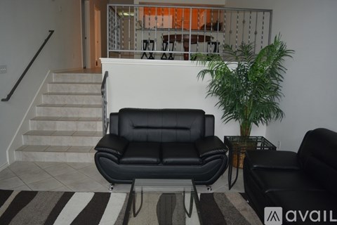 A black leather sofa sits in a living room with a striped rug and a potted plant.