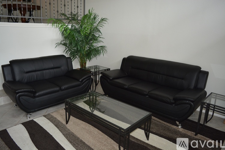 Two black leather sofas and a glass coffee table in a room.