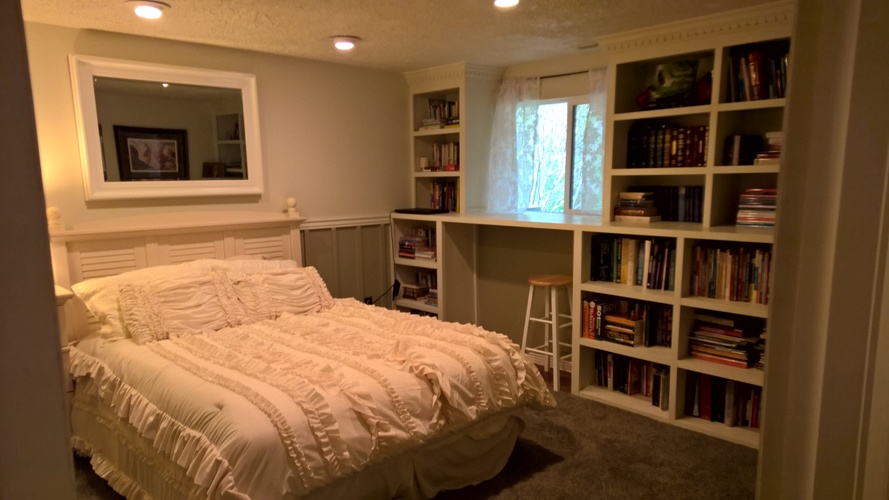 A bedroom with a bed, bookshelves, and a window.