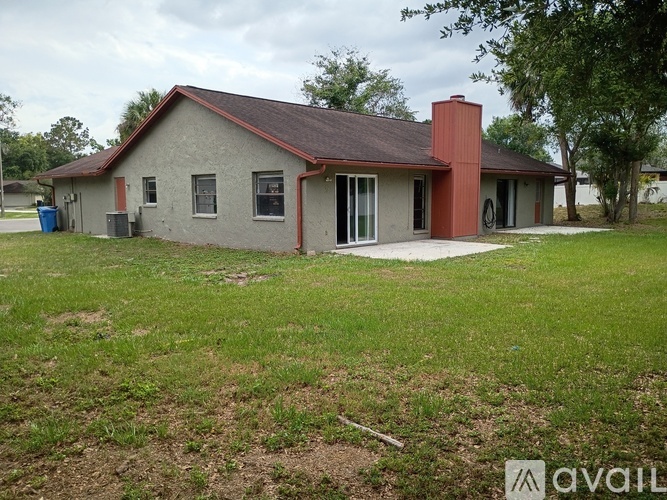 A house with a red roof and a brown chimney is surrounded by a grassy area.