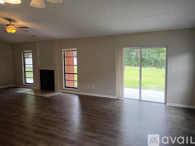 A spacious room with a ceiling fan and sliding glass doors leading to a backyard.