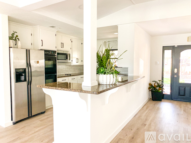 A kitchen with a refrigerator, microwave, oven, and a counter with a plant on it.