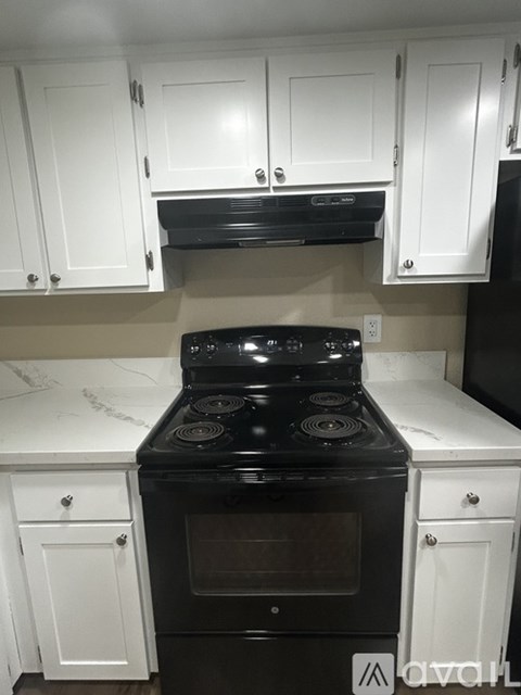 A black stove top oven in a kitchen with white cabinets.